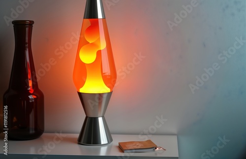 Retro orange lava lamp sits near white wall. Stylish vintage nightlight casts warm glow. Liquid wax flows inside creating beautiful patterns. Warm, cozy atmosphere. Perfect for bedroom living room. photo