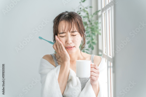 虫歯が痛い・しみて頬を押さえるアジア人女性
