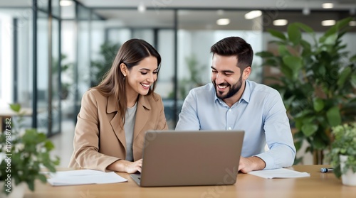 Two busy happy professional business man and woman executive leaders. Two smiling business colleagues, a woman in a light taupe/khaki jacket and a man in a light-blue button-down, are seated at a wood