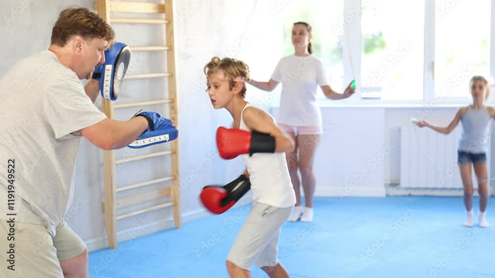 Young boy with her trainer father at gym. Boy wearing boxing gloves exercise and punch to pads for boxing Young boy with her trainer father at gym. Boy wearing boxing gloves exercise and punch to pads for boxing