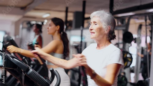 Slender athletic mature woman during cardio exercises on elliptical simulator in fitness center. Sports to max. Electronic tracking for most productive workout