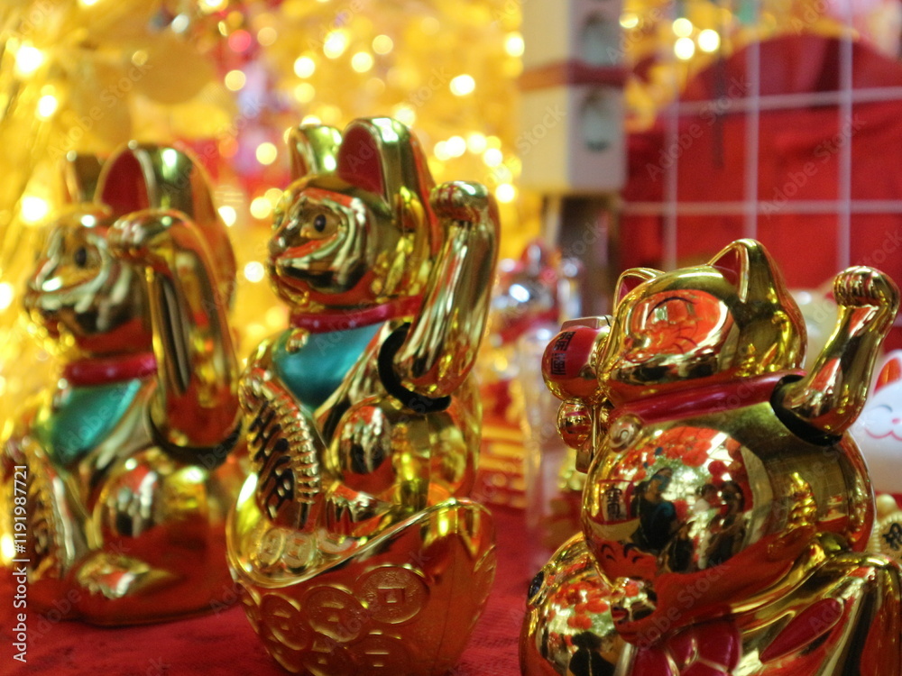 Fototapeta premium A close-up shot of several golden Maneki-neko waving cats with blurred bokeh lights in the background.
