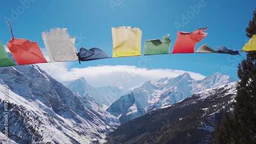 Colorful prayer flags blowing in Keylong, Lahaul, India. Buddhist Prayer Flags in Winter against snow covered Himalaya mountains. Windy cloudy day during storm.

