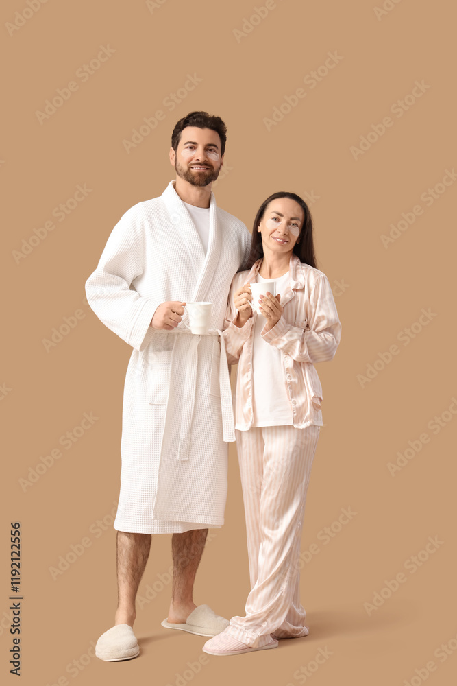 Loving couple with under-eye patches and cups of coffee on beige background Loving couple with under-eye patches and cups of coffee on beige background