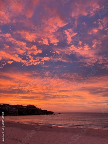 Bondi Beach Sunrise. Scattered pink, orange and purple clouds lit up by the rising sun behind the horizon. 