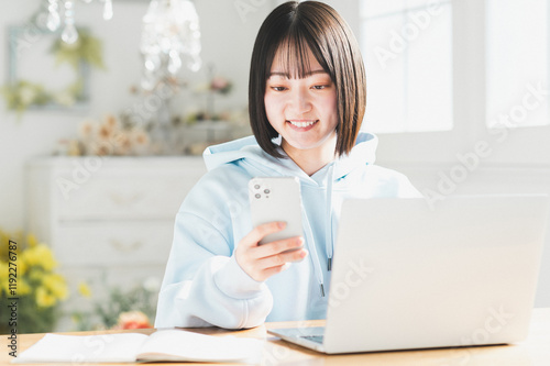 リビングでスマートフォンとノートパソコンを使う若い日本人女性