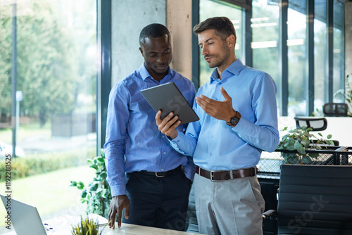 Two diverse business partners standing and discussing project working together at workspace