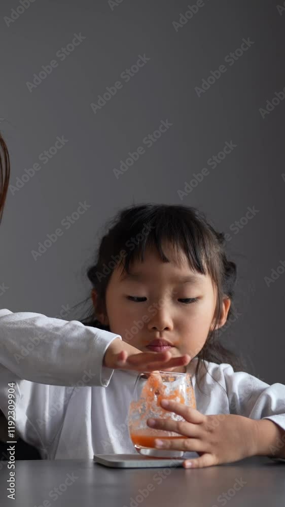 A Japanese parent and child, a woman in her 30s and a 6-year-old girl, are drinking vegetable juice in their living room, wearing simple white clothes and aprons. Vertical video. A Japanese parent and child, a woman in her 30s and a 6-year-old girl, are drinking vegetable juice in their living room, wearing simple white clothes and aprons. Vertical video.