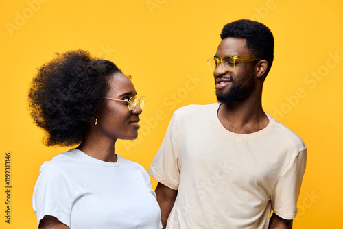 Young multi ethnic couple smiling joyfully against a vibrant yellow background, wearing stylish summer outfits and trendy sunglasses, conveying love and happiness photo