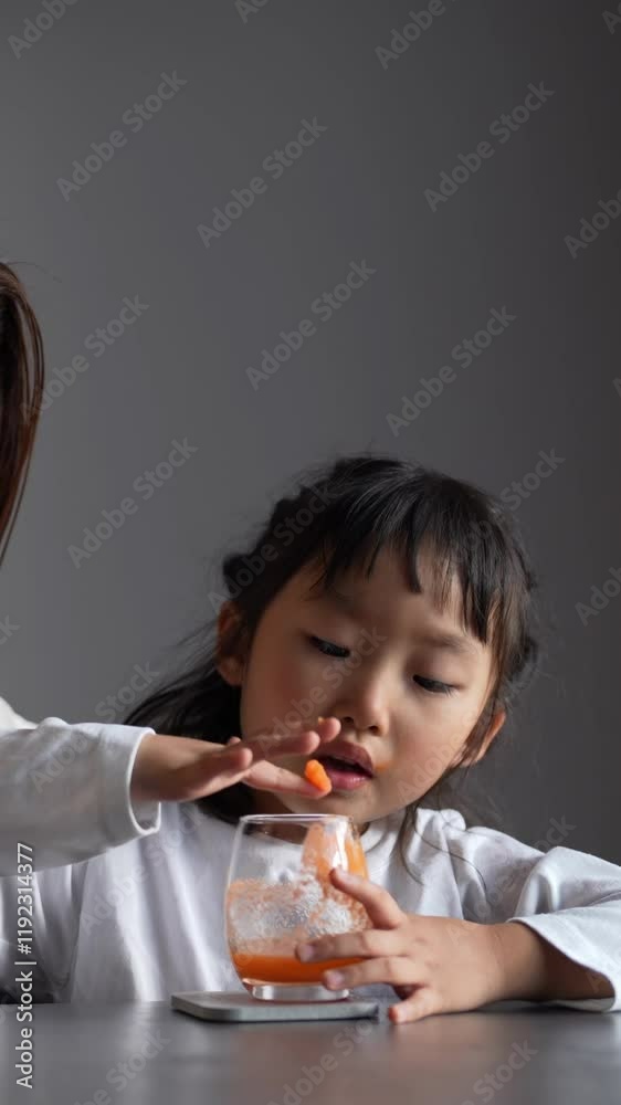 A Japanese parent and child, a woman in her 30s and a 6-year-old girl, are drinking vegetable juice in their living room, wearing simple white clothes and aprons. Vertical video. A Japanese parent and child, a woman in her 30s and a 6-year-old girl, are drinking vegetable juice in their living room, wearing simple white clothes and aprons. Vertical video.