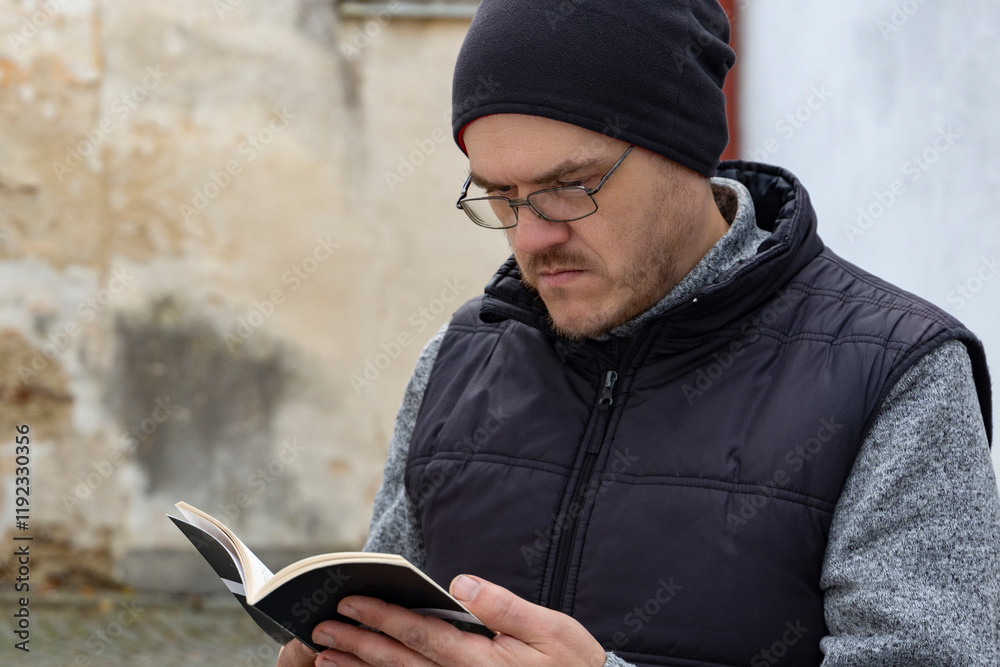 A man reading a book outdoors in an autumn city.