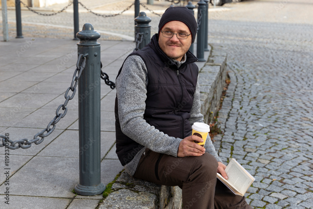 A man reading a book outdoors in an autumn city.