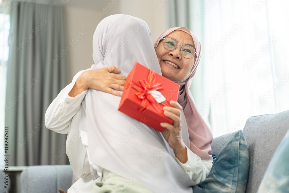 © Art_Photo - Muslim woman giving gift box to elderly mother, expressing love family bonding moment, happy holiday celebration, hijab women sharing joy, islamic cultural tradition, caring family relationship