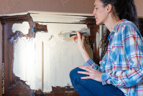 Woman restoring old furniture applying chalk paint with brush photo