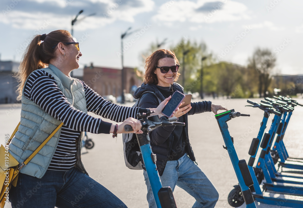 Two young women friends using an app to rent a scooter in the city. Active lifestyle