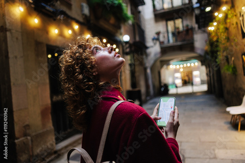 Woman holding directions on smart phone and looking up at alley photo