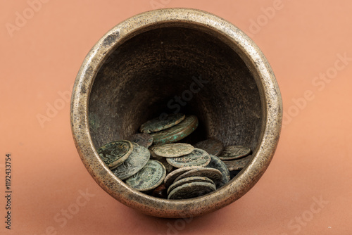 Ancient Roman coins collected inside a bronze container on an orange background. photo