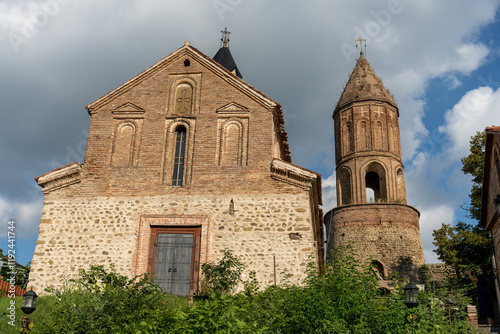 A large stone building with a steeple and a small door. The building is surrounded by bushes and trees