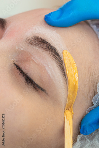 Hands of Professional Beautitian While Completing Eyebrow Correction with Wax and Wooden Sticks in Beauty Salon As Eyebrow Hair Removal with Wax.