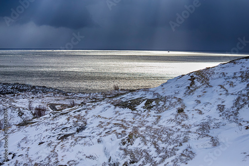 Lofotens Winter Snowy Scenery with Stony Shore in Front and Small Boat on the Background Floating Away from Shoreline. photo