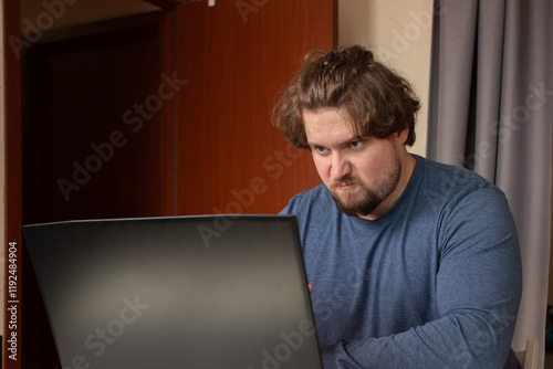Angry man working on laptop, stress from remote work, emotion-driven reaction at desk
