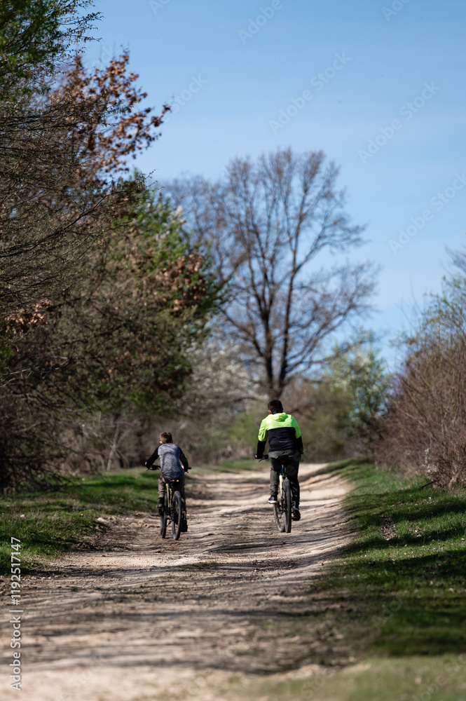A scenic view of two people cycling on a dirt road, surrounded by trees and greenery under a bright sky. The atmosphere is peaceful and serene. A scenic view of two people cycling on a dirt road, surrounded by trees and greenery under a bright sky. The atmosphere is peaceful and serene.