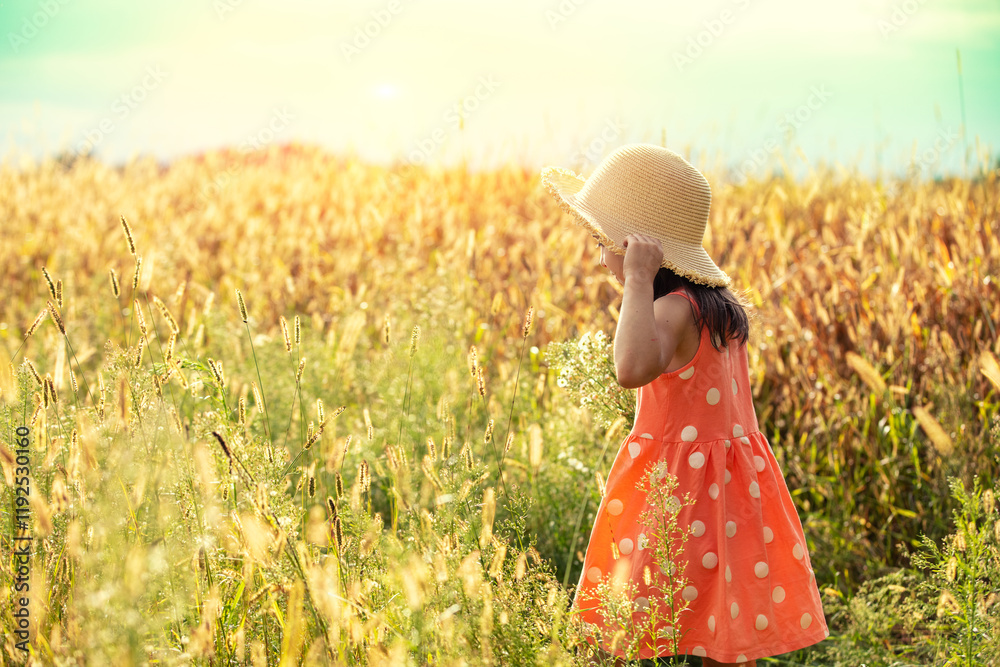 Happy little girl in a straw hat walking in the wheat field on a sunny summer day