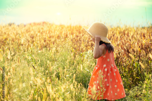 Obraz na płótnie Happy little girl in a straw hat walking in the wheat field on a sunny summer day w salonie
