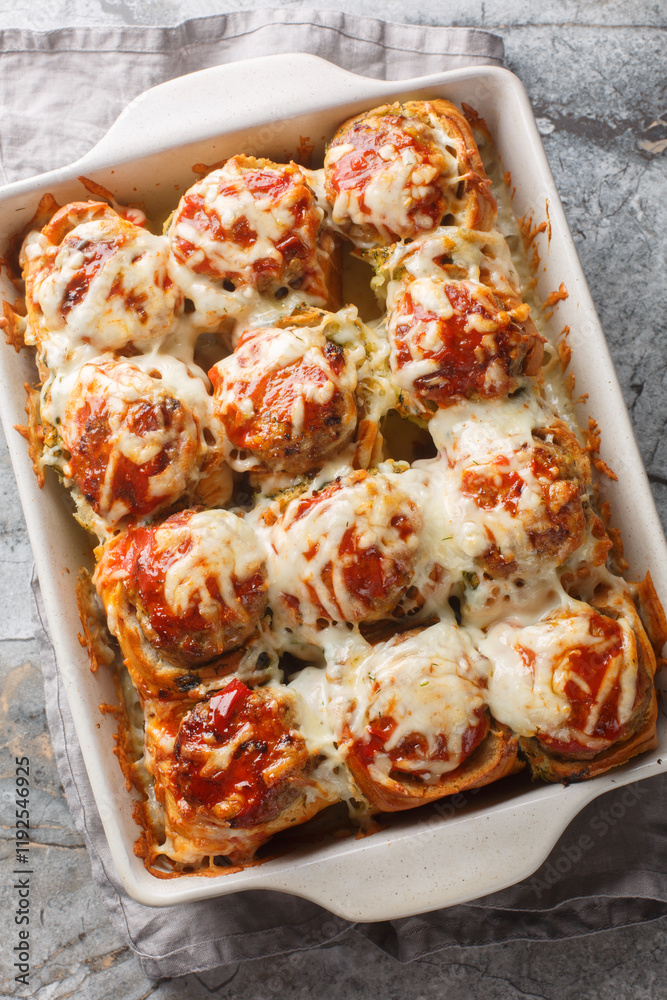 Meatball Stuffed Garlic Bread Sliders topped with cheese closeup on the baking dish on the table. Vertical top view from above