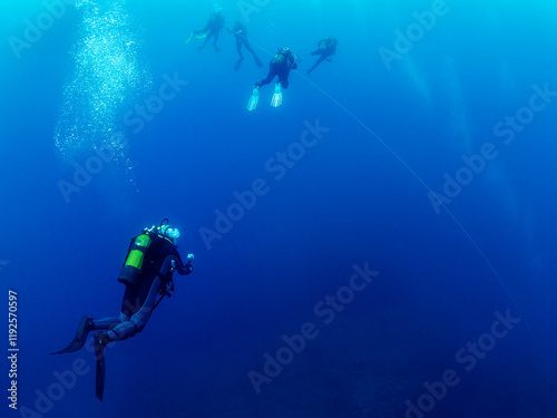 group of scuba divers in wetsuit diving holding on to the anchor line while making the safety stop before rising to the surface, concept of active leisure and underwater adventure, copyspace for text