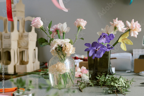 Medium close up of pastel pink roses and purple orchid in crustal vase on table covered with fresh and green ruscus photo