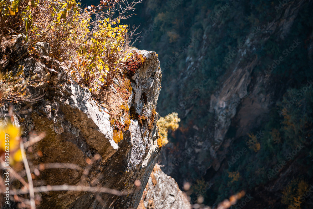 Obraz premium A dramatic cliff edge in Yunnan, China, showcasing rugged rock formations and autumnal foliage clinging to the precipice. The Dali region's unique landscape is visible in the deep shadows of the vall