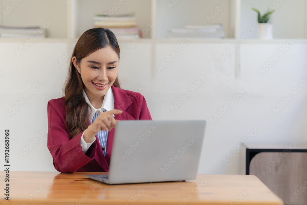 Smiling Asian accountant working with calculator and analyzing financial documents on laptop at table surrounded by documents on table Smiling Asian accountant working with calculator and analyzing financial documents on laptop at table surrounded by documents on table