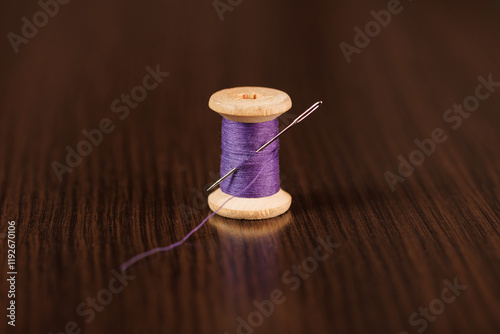 A sewing needle with a large eye is stuck into a spool of purple thread. Selective focus.