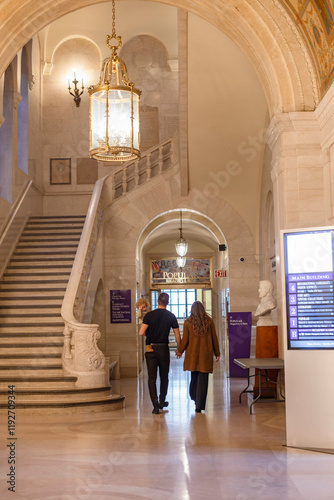 A couple walks through an elegant hallway with arched ceilings and a hanging chandelier. Cleveland Public Library, Ohio, USA photo