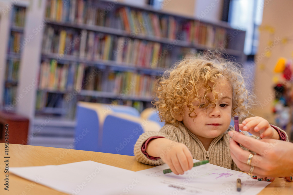A curly-haired toddler engaging in coloring activity at a table with adult assistance in a library. Cleveland, Ohio, USA A curly-haired toddler engaging in coloring activity at a table with adult assistance in a library. Cleveland, Ohio, USA