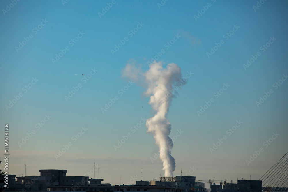 Chimney of a central heat and hot water plant in urban area. Urban plant provides heating and hot water to the buildings of the city Chimney of a central heat and hot water plant in urban area. Urban plant provides heating and hot water to the buildings of the city