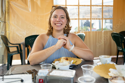 Smiling woman sitting at a cafe table with a cup of coffee and a croissant, Netherlands