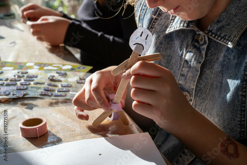 A child engages in arts and crafts, creating a puppet with colored sticks and decorative materials at a sunlit table, Netherlands photo