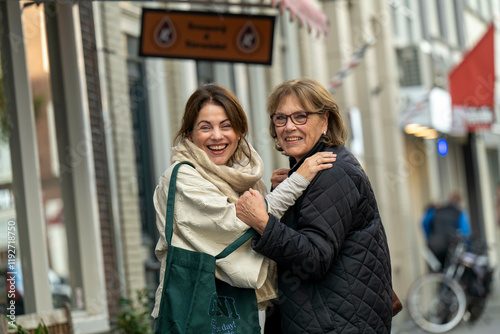 Two women share a joyful embrace on a lively city street, smiling broadly and engaged in animated conversation, Netherlands photo