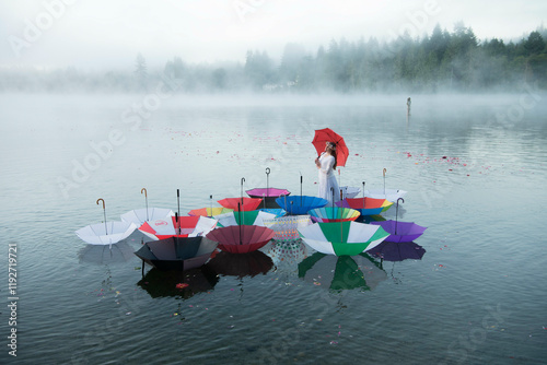 A serene lake scene with various colorful umbrellas floating on the water. Mist envelops the background as a lone figure in white holds a red umbrella, Wildcat Lake, WA, USA photo