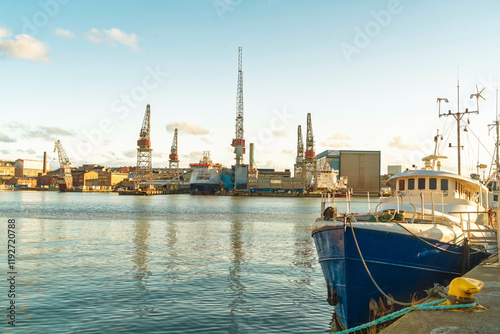 A serene harbor scene in Helsinki with a blue boat in the foreground and industrial cranes in the distance under a clear sky, Finland photo