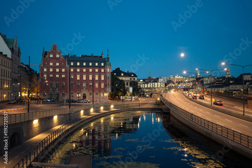 Twilight cityscape with historical buildings reflected in the calm waters of a canal in Gamla Stan, under a clear sky with a bright full moon, Stockholm, Sweden