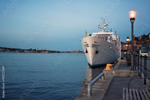 A cruise ship docked in a calm harbor during twilight with a lamppost and bench in the foreground in Sodermalm, Stockholm, Sweden