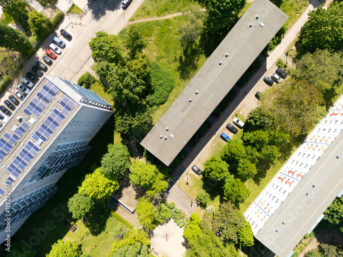 Aerial view of a modern building with a solar-paneled roof beside traditional rooftops surrounded by lush green trees and parked cars, Berlin, Germany photo