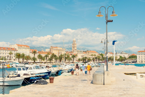 Sunny day at a Mediterranean marina with boats docked, people strolling, and historic buildings in the background, Split, Croatia. photo