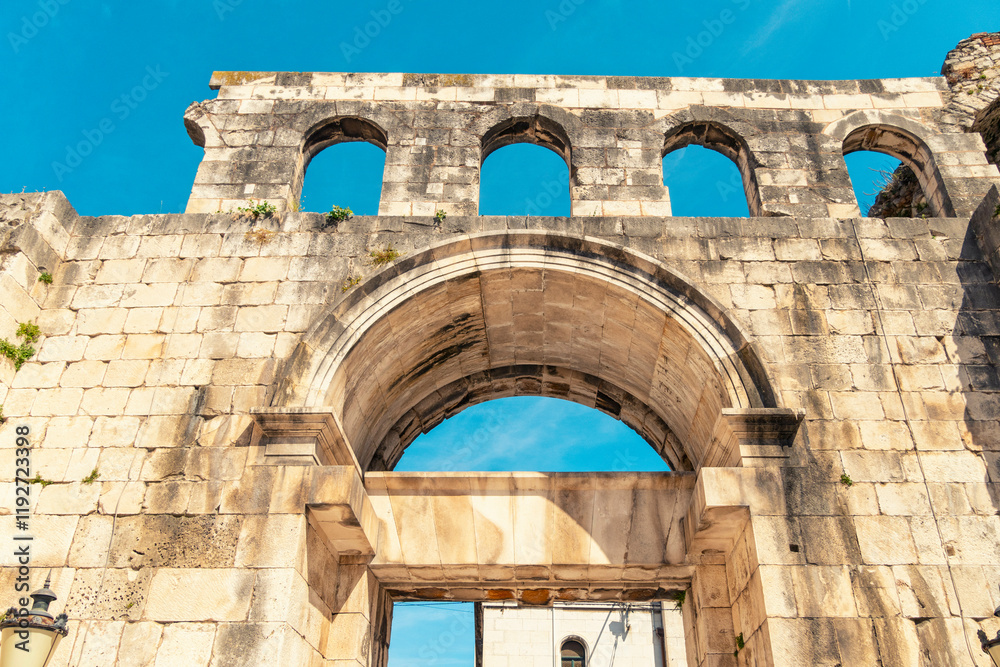 Silver Gate ancient stone archway under a clear blue sky with visible architectural details and vegetation growth, Split, Croatia