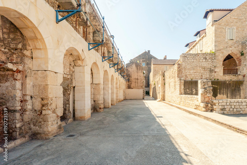 Sunlit cobblestone alley flanked by old buildings  and Ethnographic Museum with arches in historic Split, Croatia