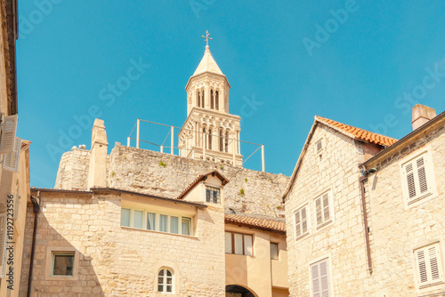 Sunlit stone buildings with a towering bell tower of St Domnius Cathedral against a clear blue sky, Split, Croatia photo