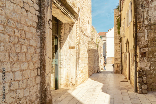 Narrow cobblestone street with ancient stone buildings and a clear blue sky in a historic Split, Croatia photo